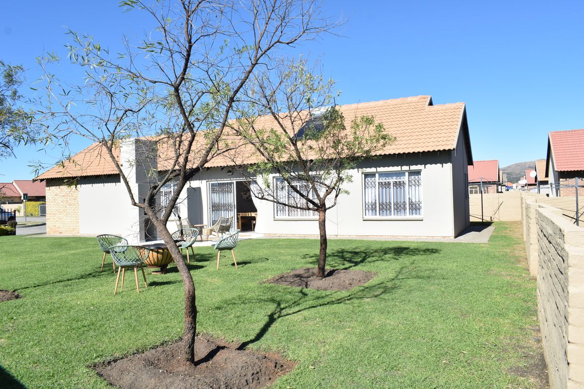 Rear view of the house featuring a tiled roof with solar water heater, security bars on windows, and a well-maintained lawn area.