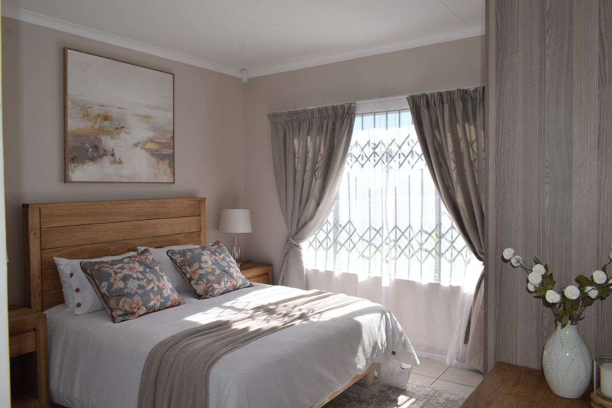 A well-maintained bedroom featuring neutral tones, tiled flooring, and a built-in wardrobe with a secure window gate.