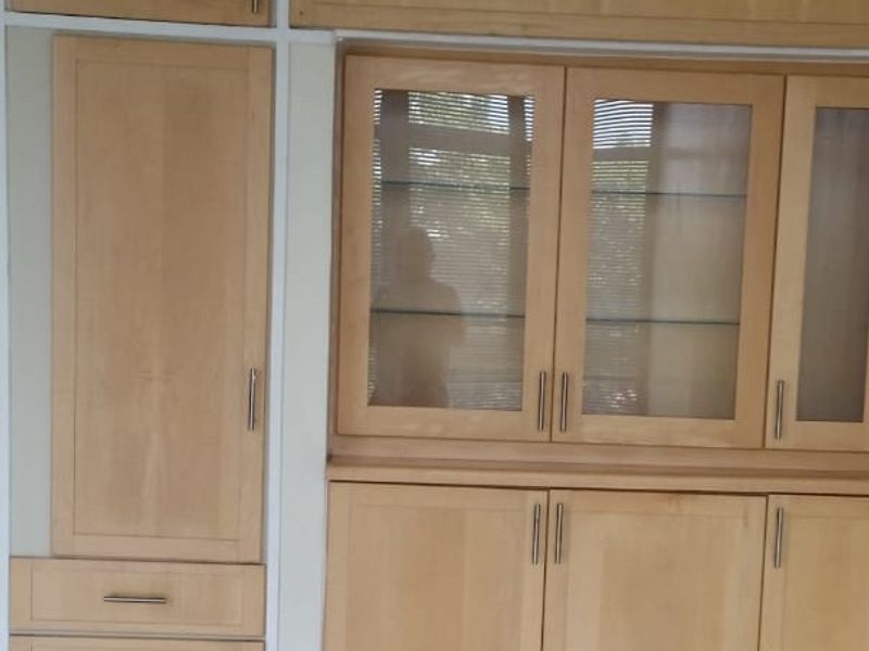A wall of light wood built-in cabinetry featuring a mix of solid doors, drawers, and glass-fronted display units.