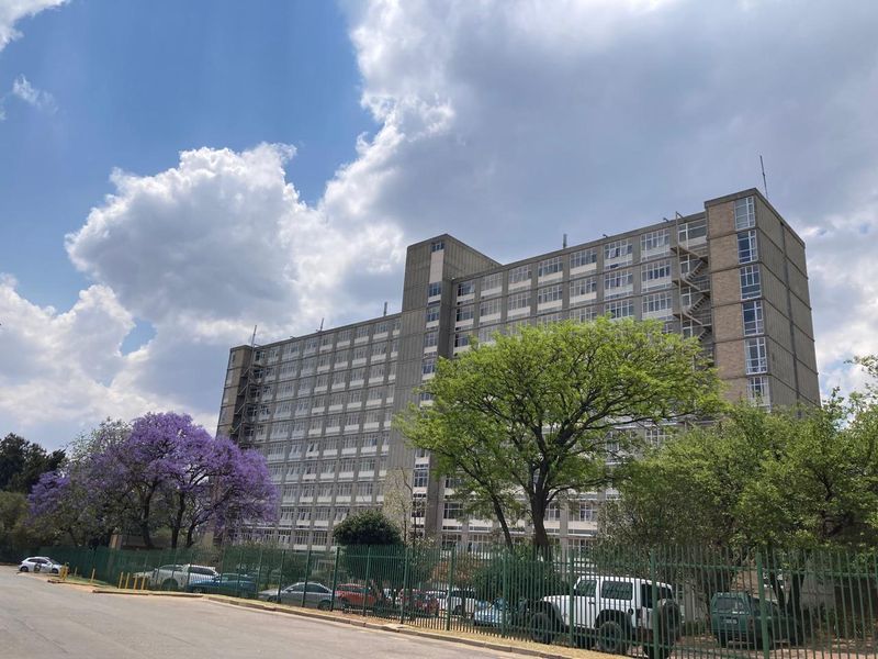 A multi-story apartment building facade featuring a grid of windows, external fire escapes, and secure perimeter fencing.