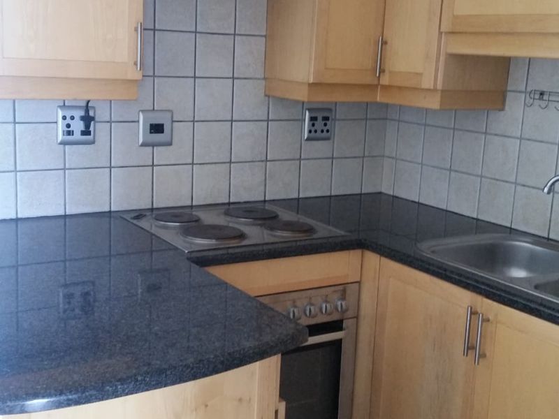 A functional kitchen featuring light wood cabinetry, dark granite countertops, a built-in electric hob, oven, and extractor fan with tiled backsplash.