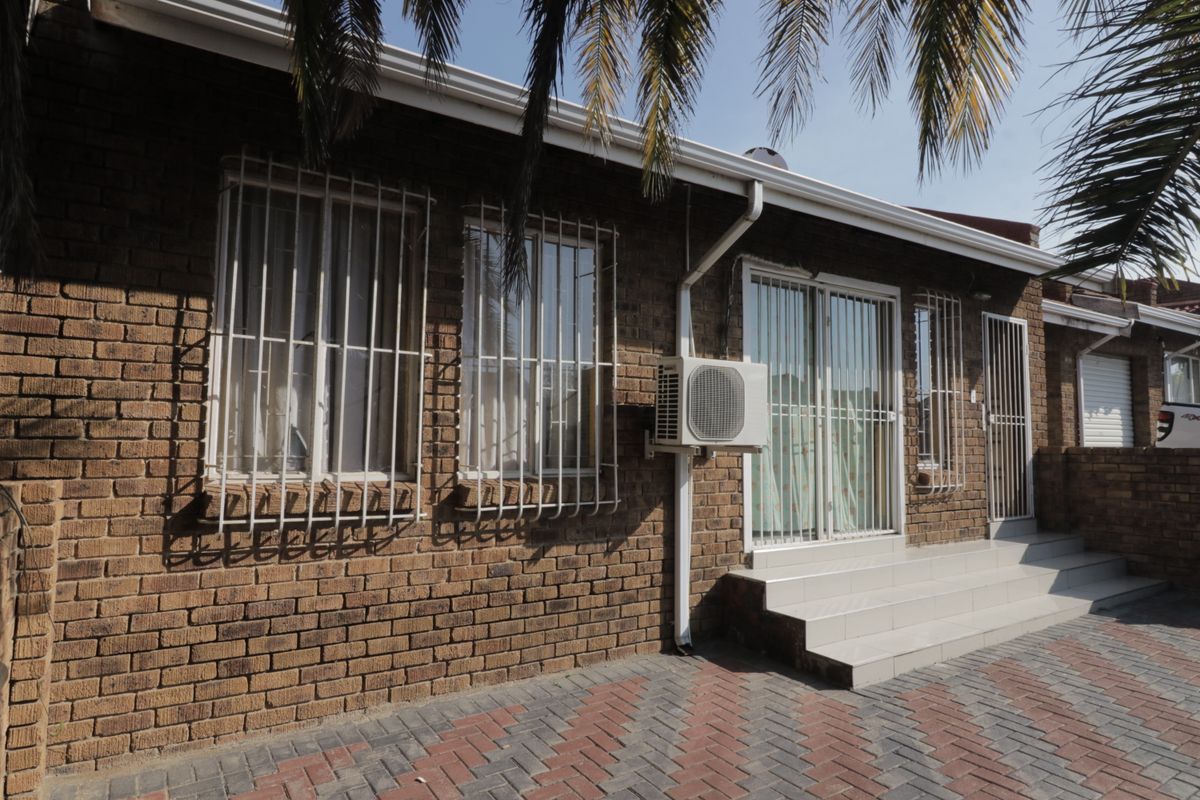 Exterior view of a brick-faced house featuring security bars on windows, a paved patio area, and an external air conditioning unit.