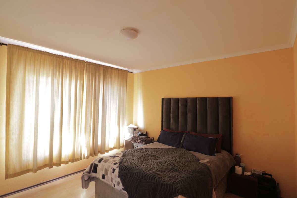 A bedroom featuring laminate flooring, neutral wall tones, and large windows with curtains, providing a functional and comfortable sleeping space.