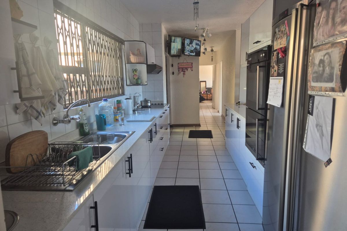 A galley-style kitchen featuring white cabinetry, a double sink, built-in oven, and tiled flooring, leading into a hallway.