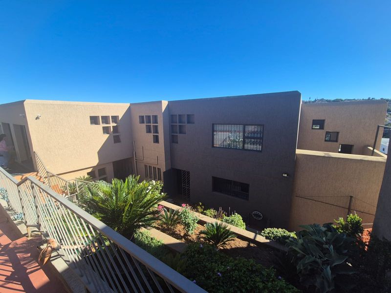 A view of the rear exterior facade featuring textured walls, security-fitted windows, and a terraced garden area with a metal balcony railing.