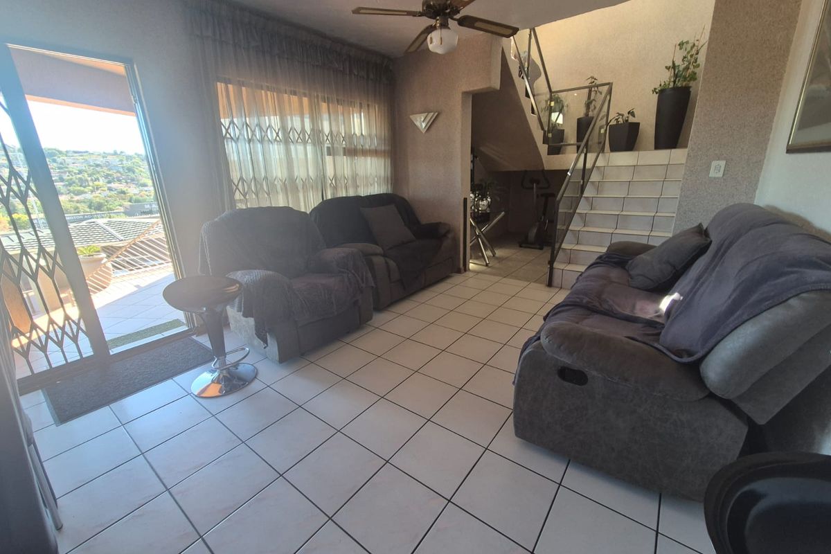 Spacious living area featuring tiled flooring, a ceiling fan, and a staircase with a glass balustrade, leading to an outdoor balcony.