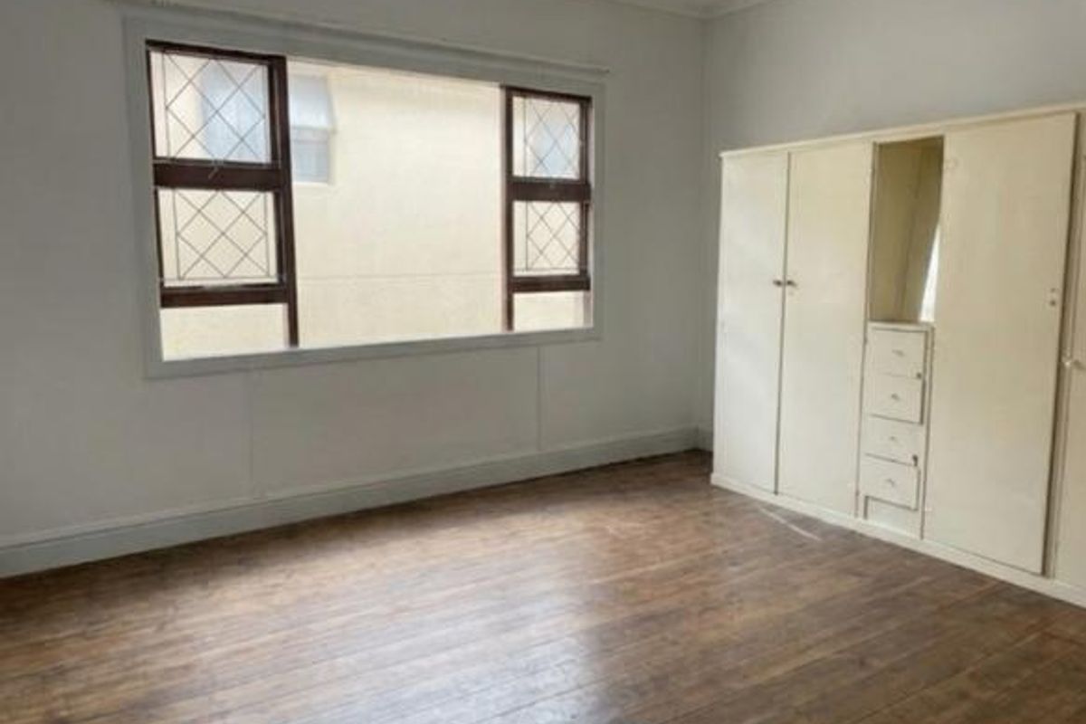 A vacant bedroom featuring original timber flooring, a built-in wardrobe with integrated mirror, and a character leaded glass window.