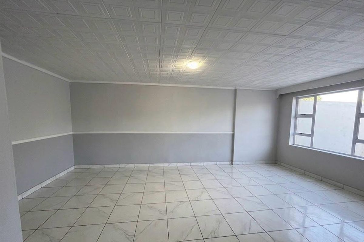 A bright, empty living room featuring neutral grey walls, a decorative tiled ceiling, and modern white marble-look floor tiles.