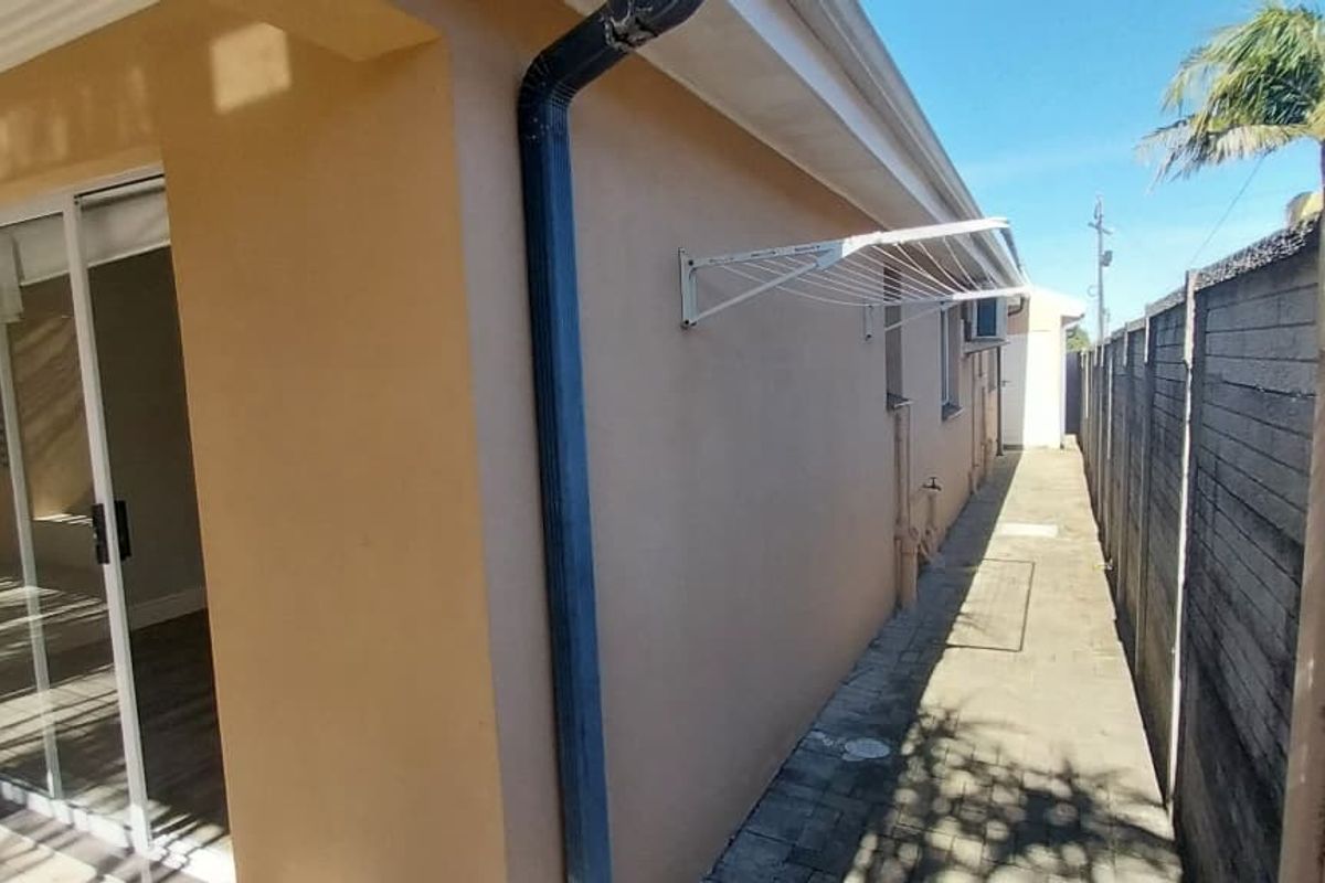 A side exterior view of the townhouse featuring a paved walkway, boundary wall, and a wall-mounted drying rack.