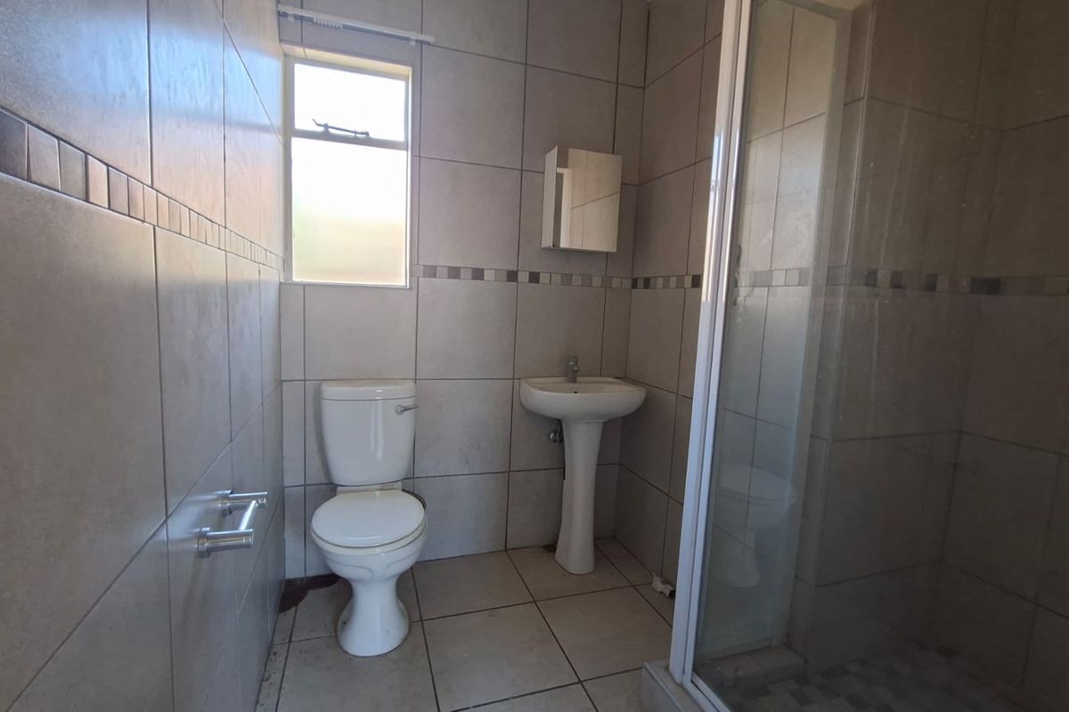 A functional bathroom featuring a pedestal basin, toilet, and a glass-enclosed shower with neutral wall and floor tiling.