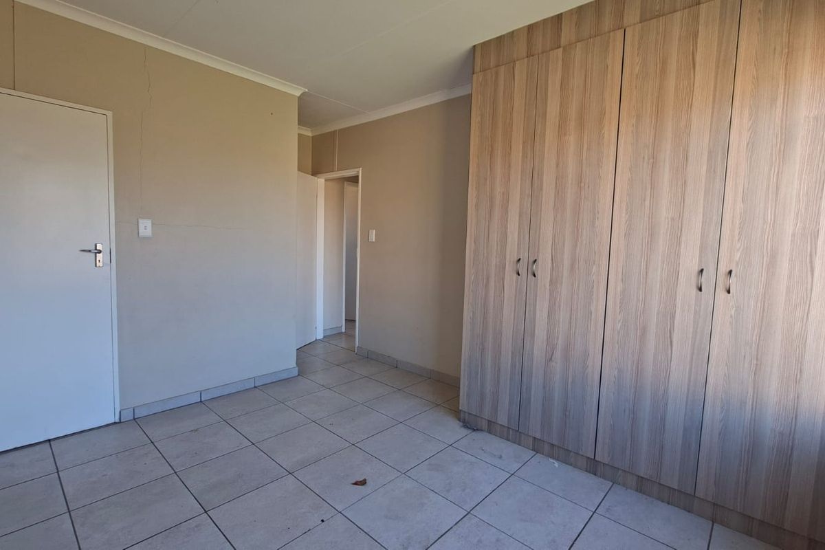 A vacant bedroom featuring neutral tiled flooring and extensive built-in wooden cupboards, providing ample storage space.