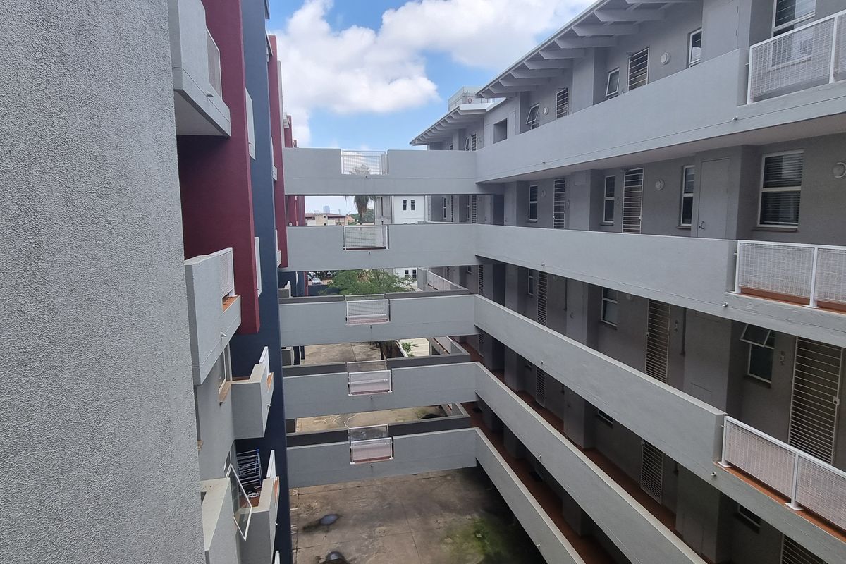 View of the apartment complex exterior showing multi-story walkways, connecting bridges, and building facade with security gates.