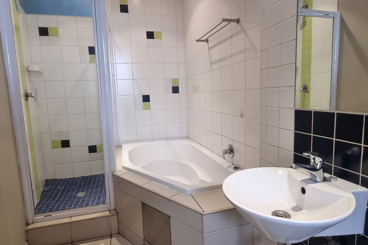 A functional bathroom featuring a corner bathtub, separate shower enclosure, and a pedestal washbasin with tiled finishes.