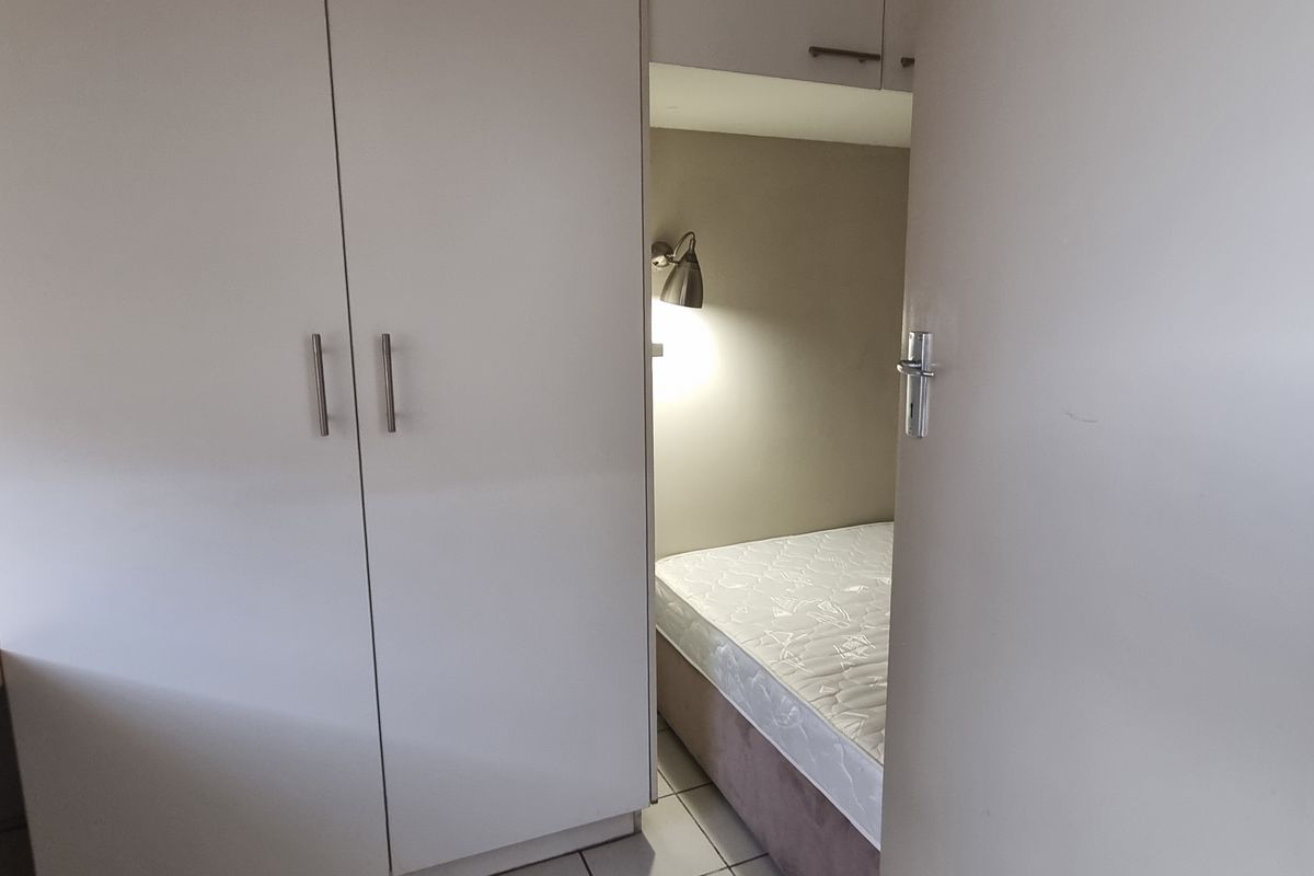 A compact bedroom featuring built-in cupboards, a fitted desk area, and tiled flooring, providing functional storage and workspace.