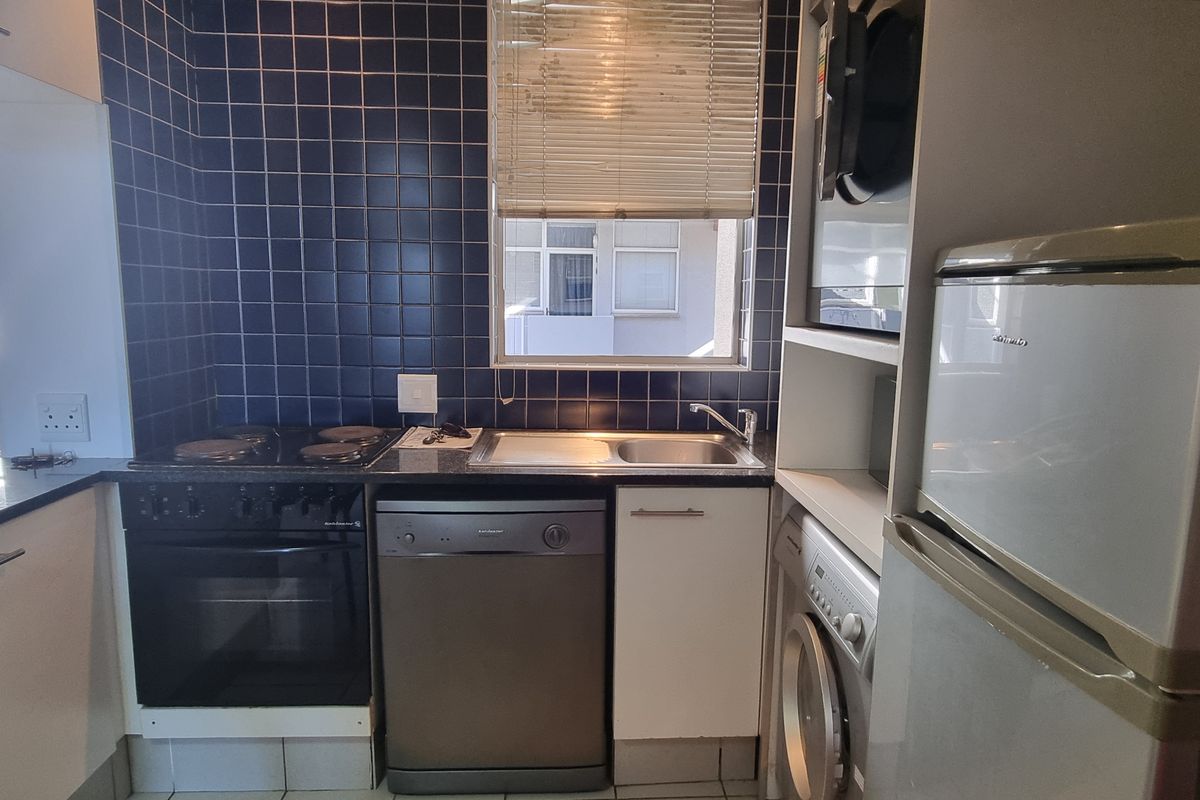 Compact kitchen featuring built-in cabinetry, electric hob, oven, and integrated dishwasher with a blue tiled splashback and functional layout.