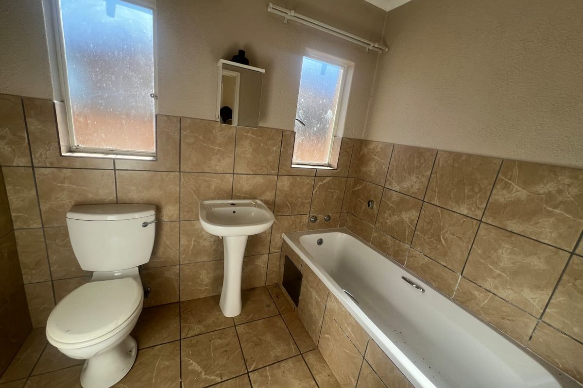 A functional bathroom featuring a pedestal basin, toilet, and bathtub with neutral floor-to-ceiling tiling and frosted windows for privacy.