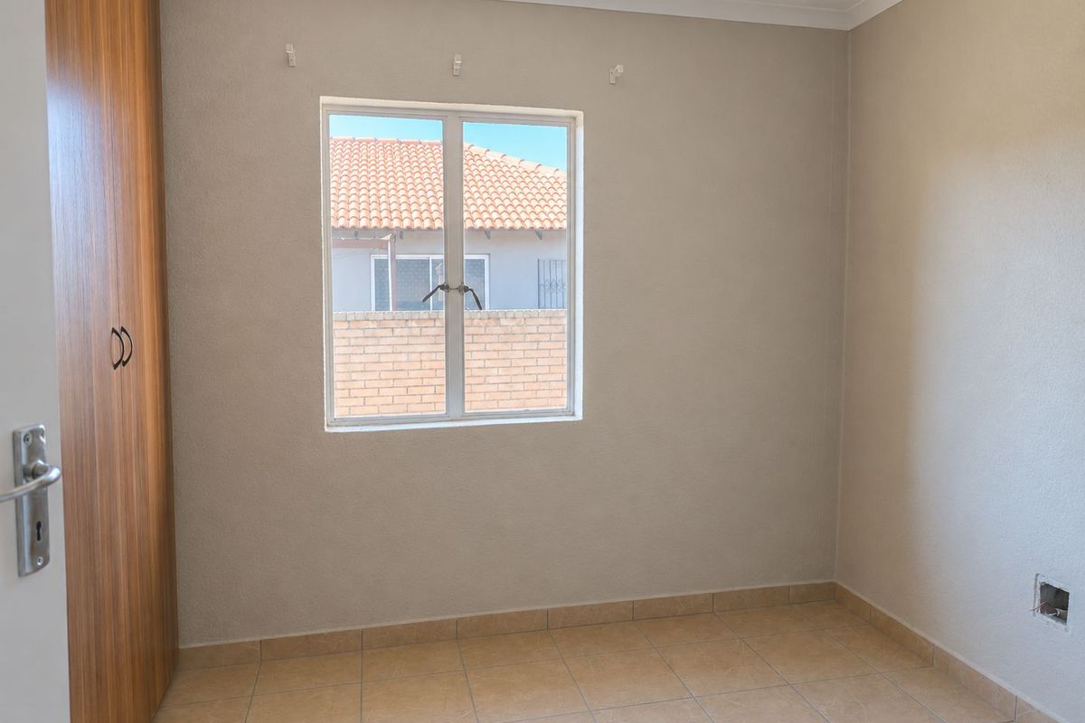 An empty bedroom featuring tiled flooring and a built-in wooden wardrobe.