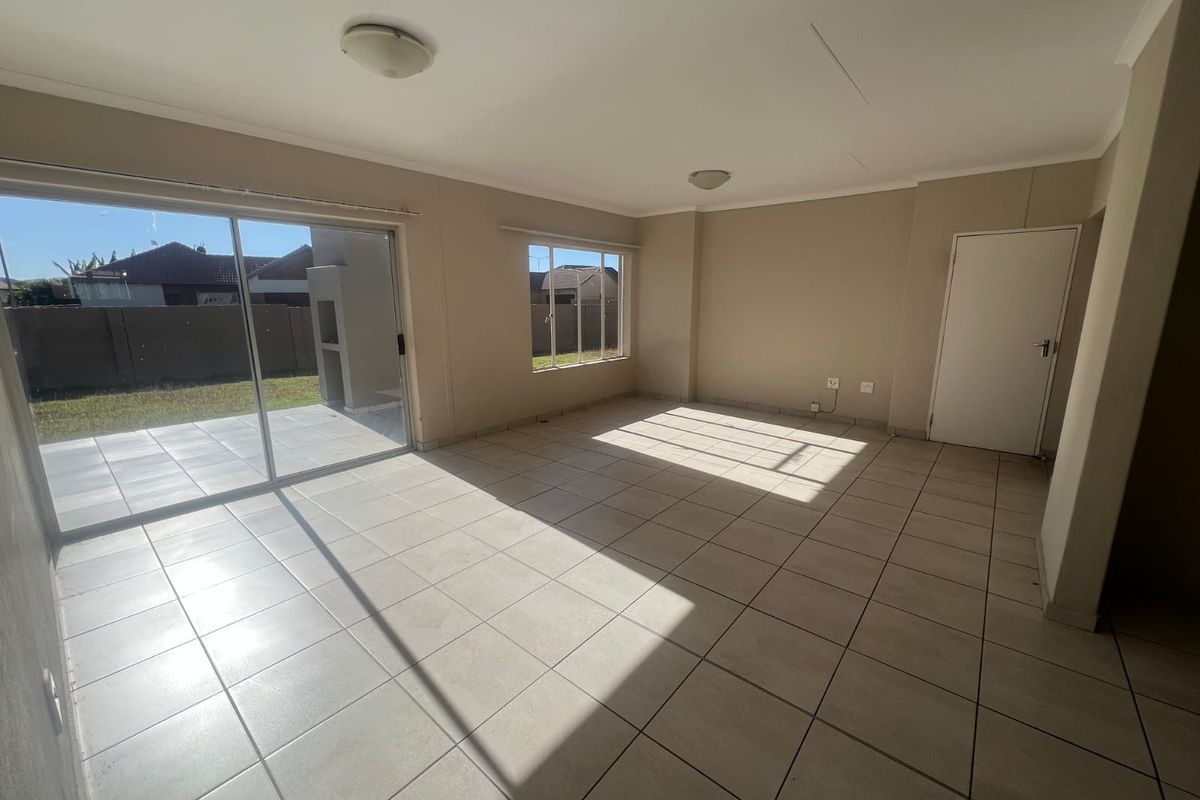 A bright, open-plan living area featuring neutral tiled flooring, large sliding glass doors leading to the patio, and ample natural light.
