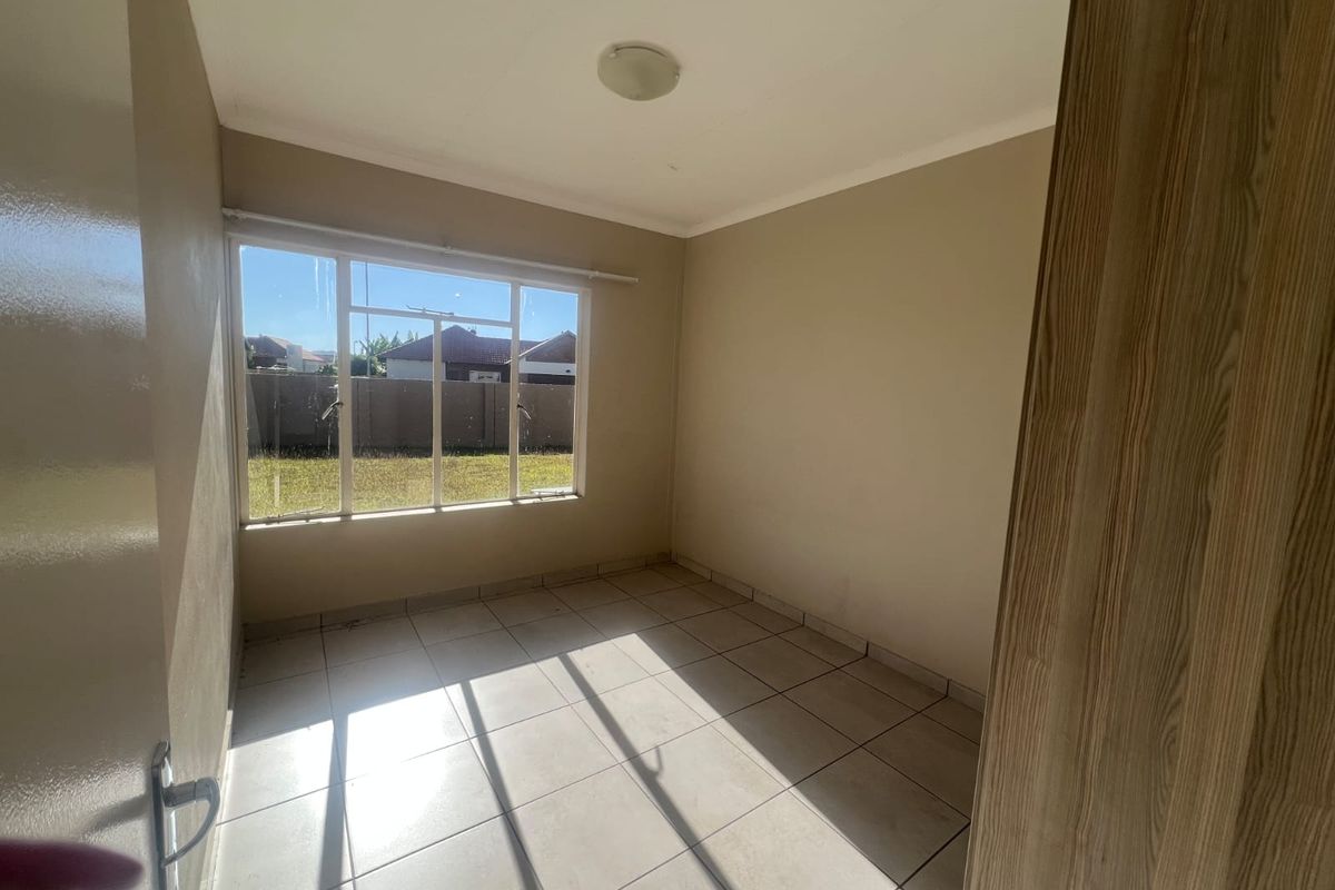 A bright, empty bedroom featuring neutral tiled flooring, a built-in cupboard, and a large window providing natural light.
