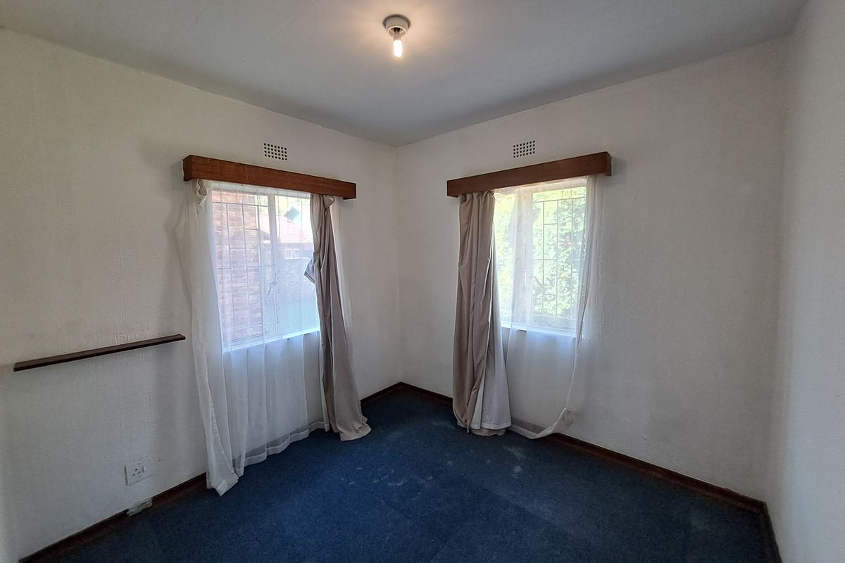 A vacant bedroom featuring blue carpet flooring, timber curtain pelmets, and security bars on the windows, offering a blank canvas for renovation.