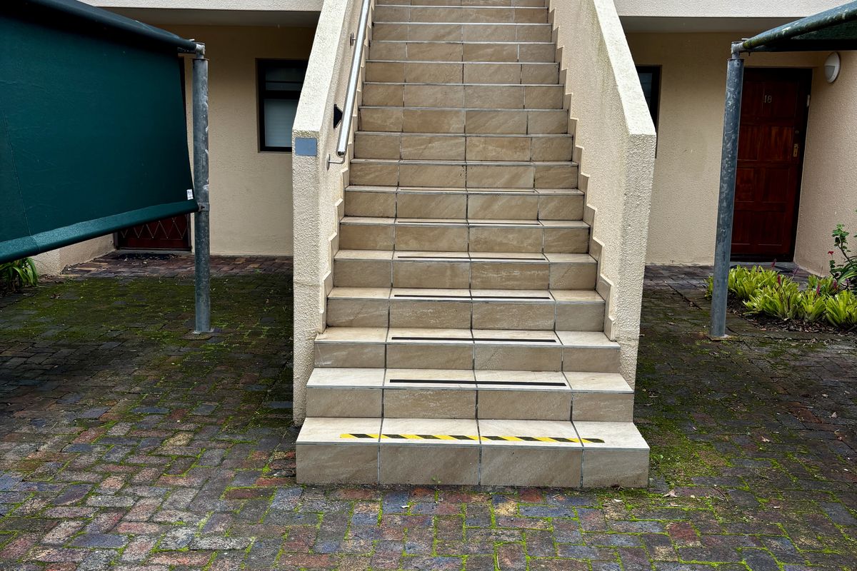Exterior view of an apartment complex featuring a central tiled staircase leading to upper-level units, set within a paved courtyard area.