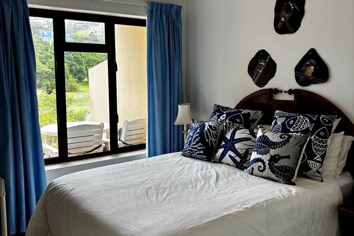 A well-maintained bedroom featuring laminate flooring, a ceiling fan, and large windows providing natural light and access to an outdoor balcony area.