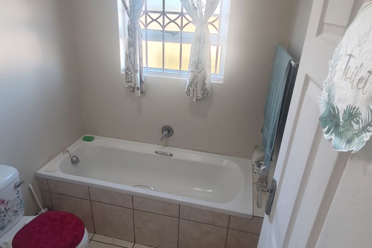 A functional bathroom featuring a bathtub with tiled surround, a toilet, and a window with security bars.