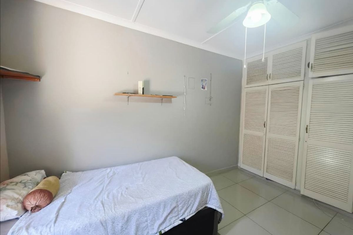 A bedroom featuring tiled flooring, a ceiling fan, and white louvered built-in cupboards providing ample storage space.