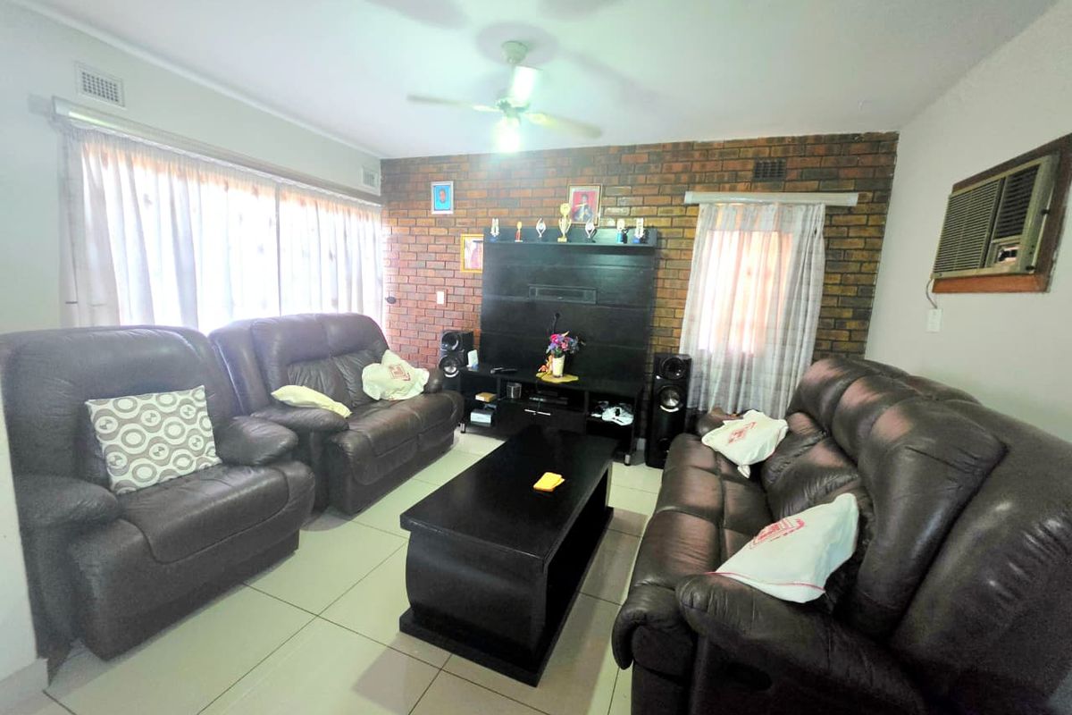 A living room featuring an exposed brick feature wall, tiled flooring, a ceiling fan, and a built-in wall air conditioning unit.