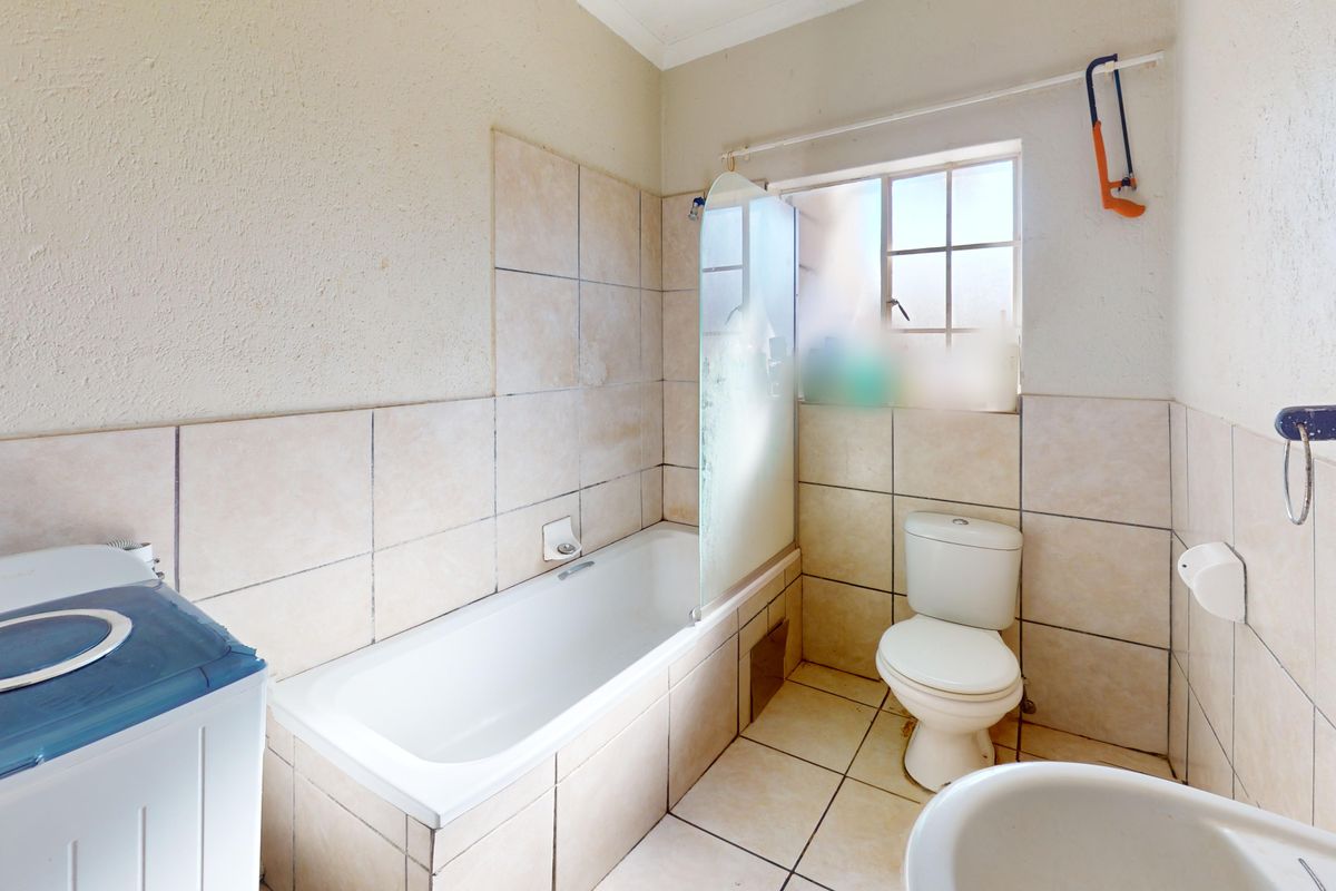 A functional bathroom featuring a bathtub with a glass screen, toilet, and tiled finishes. The space would benefit from cosmetic updates and maintenance.