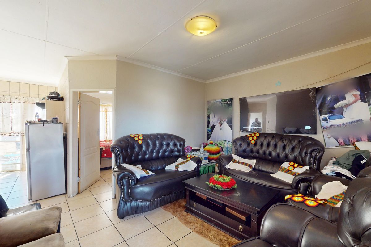 A living room featuring tiled flooring and a central ceiling light fixture, with an adjacent doorway leading to another room.