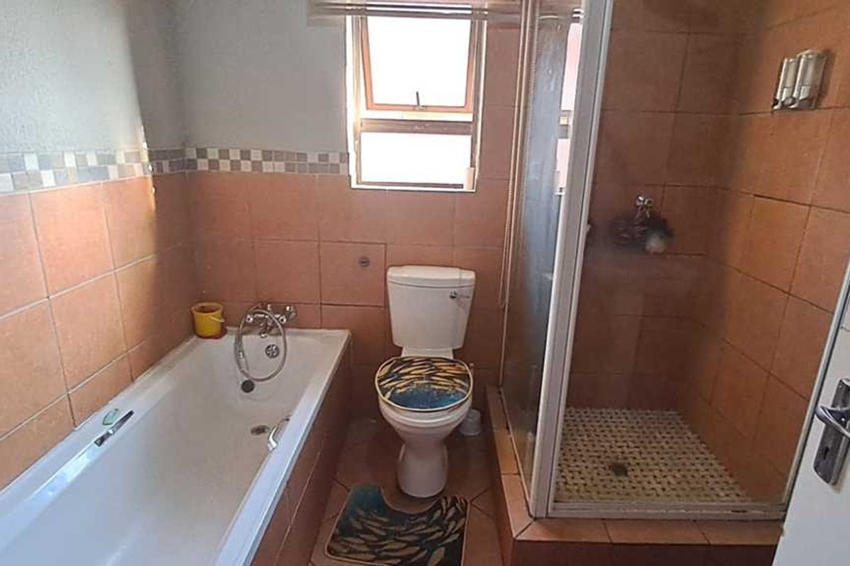 A functional bathroom featuring a bathtub, separate shower enclosure, and toilet with dated wall and floor tiling.