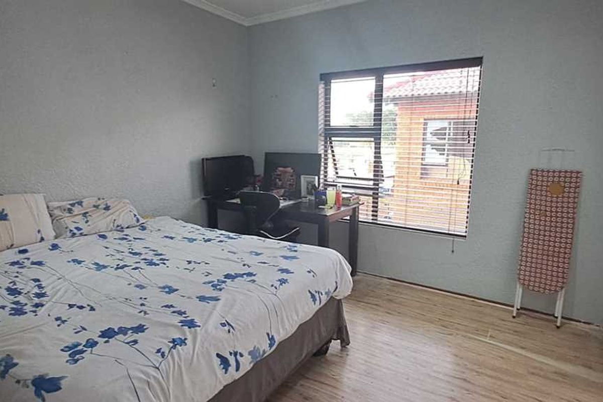 A functional bedroom featuring laminate flooring, built-in cupboards, and an aluminium window with venetian blinds.