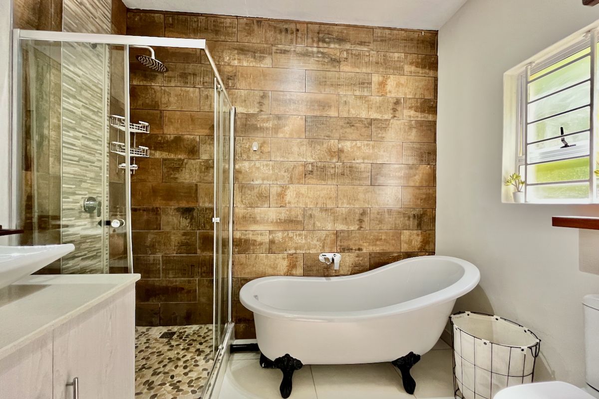 Modern bathroom featuring a freestanding clawfoot bathtub, a separate glass-enclosed shower with a rain shower head, and stylish wood-look feature wall tiling.