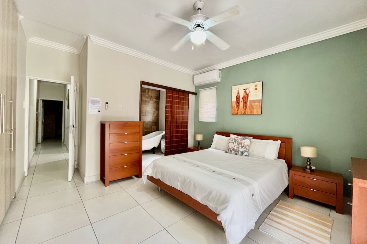 Spacious bedroom featuring tiled flooring, crown molding, a ceiling fan, and a split-system air conditioner, with an adjoining en-suite bathroom visible through a sliding door.
