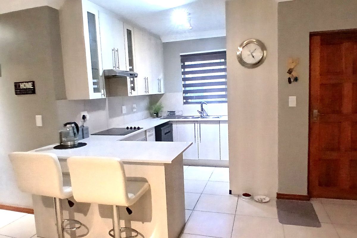 A functional kitchen featuring modern cabinetry, stone countertops, an electric hob with extractor, and tiled flooring, seamlessly integrated into the living space.