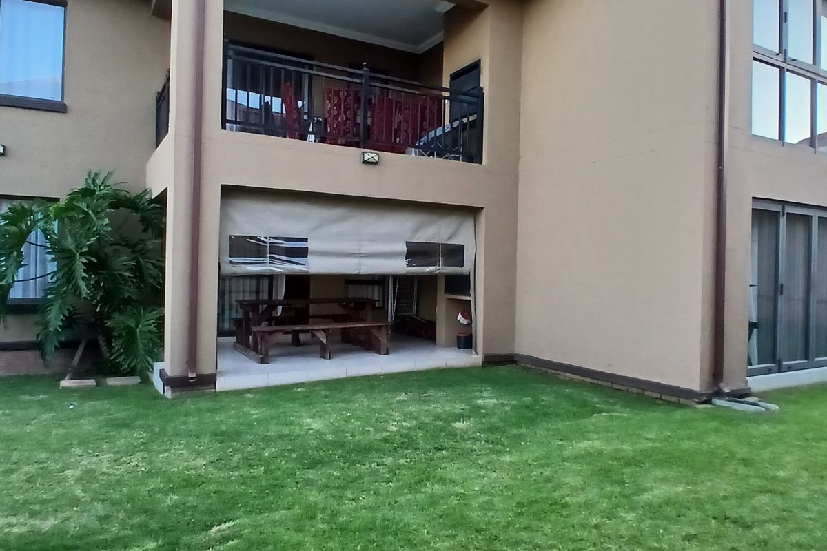 Rear view of the townhouse featuring a covered patio with a roller blind, an upper-level balcony, and a private lawn area.