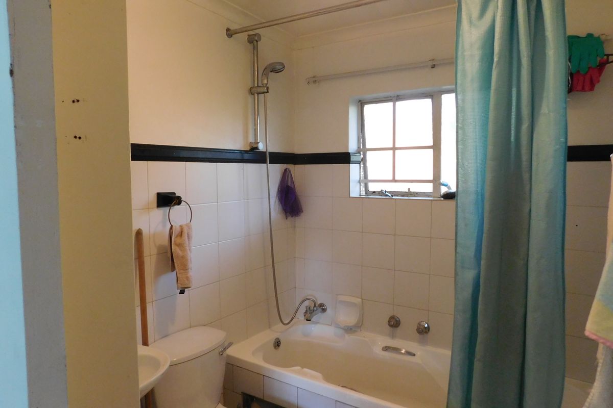 A dated bathroom featuring a built-in bathtub with shower attachment, ceramic wall tiling, and standard sanitary ware.