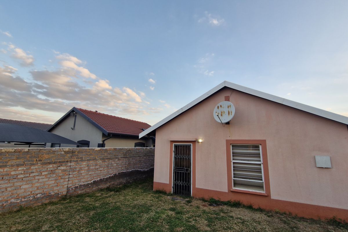 Rear view of the property featuring a brick boundary wall, security gate, and louvre window with a satellite dish mounted on the exterior wall.