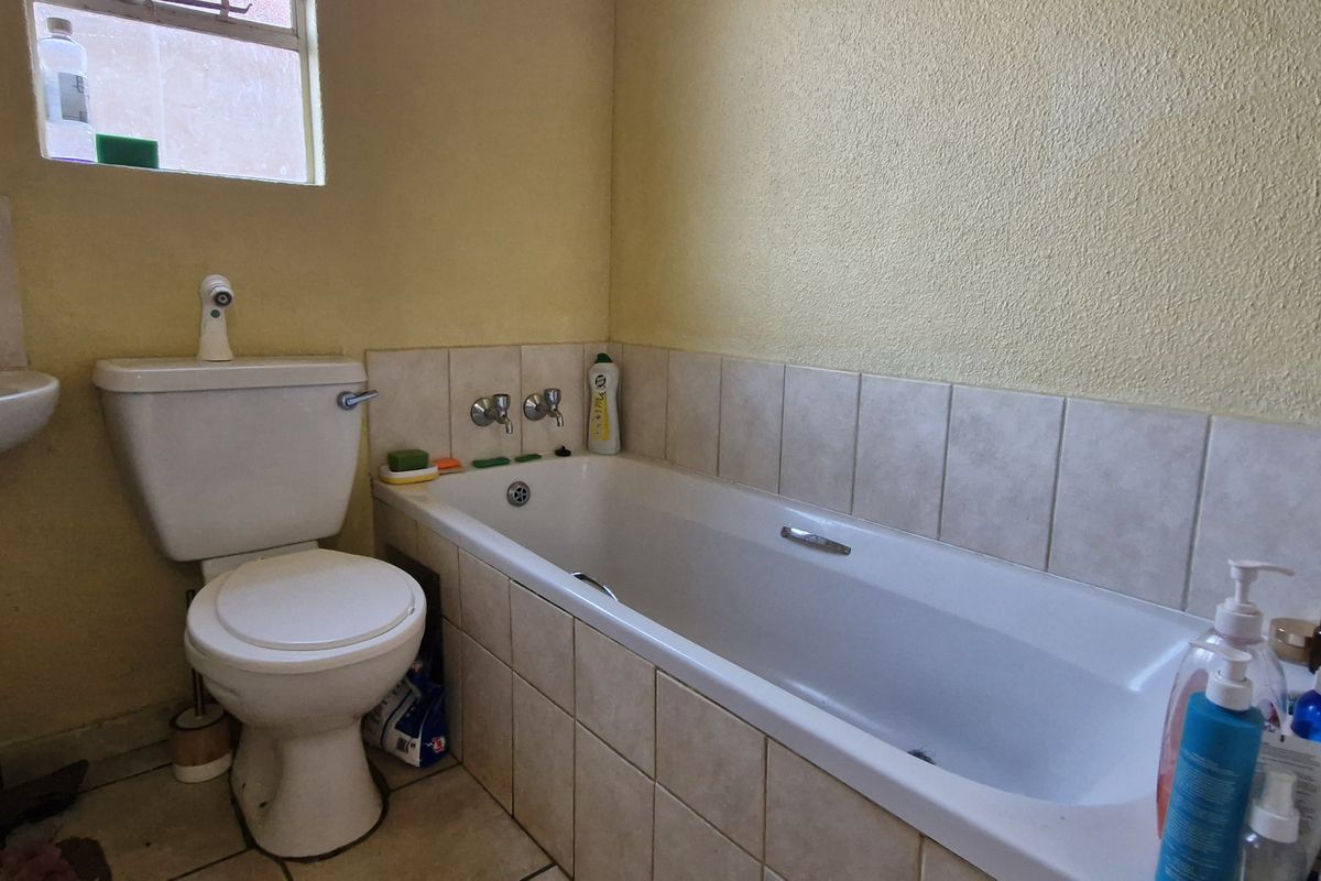 A functional bathroom featuring a standard bathtub, toilet, and wall-mounted basin with tiled splashbacks and flooring, requiring cosmetic updates to modernize the space.