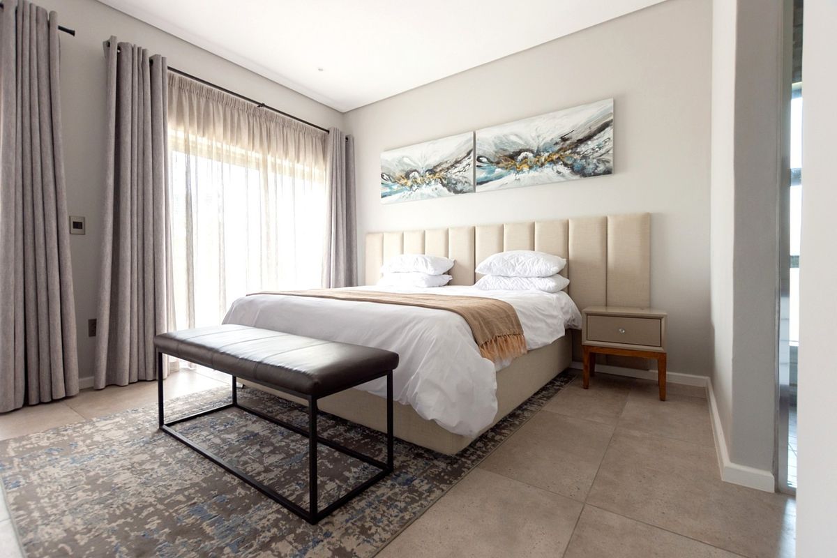 A well-maintained bedroom featuring neutral tiled flooring, recessed ceiling lighting, and a large sliding glass door providing natural light.