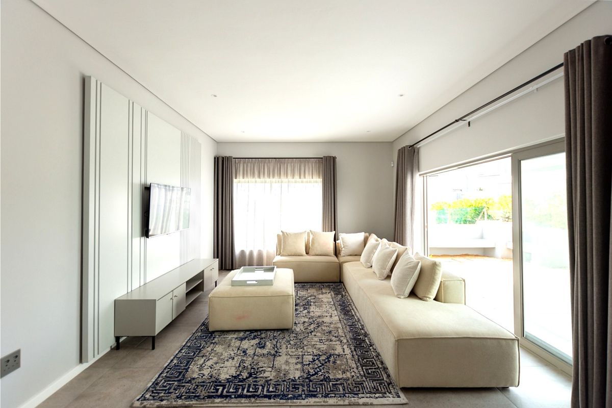 A bright and modern living room featuring a decorative feature wall, large sliding glass doors leading to an outdoor area, and neutral tiled flooring.
