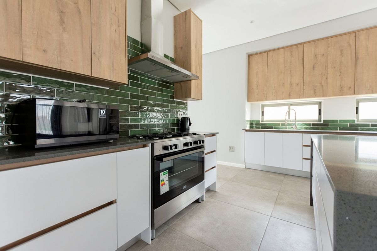Modern kitchen featuring wood-tone and white cabinetry, green subway tile backsplash, stone countertops, and high-quality stainless steel gas stove and extractor fan.