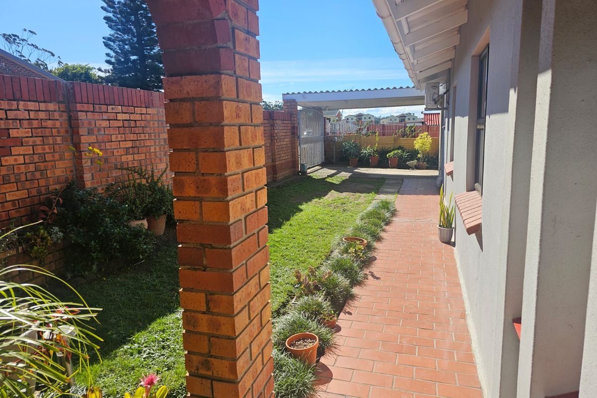A side garden pathway featuring red brick paving, a brick pillar, and a lawn area leading towards a rear carport.