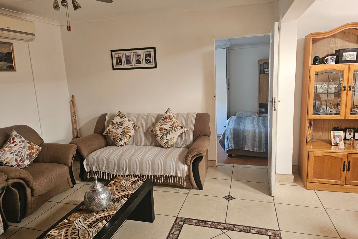 A living room featuring tiled flooring and a ceiling fan, with an open doorway leading into an adjacent bedroom.