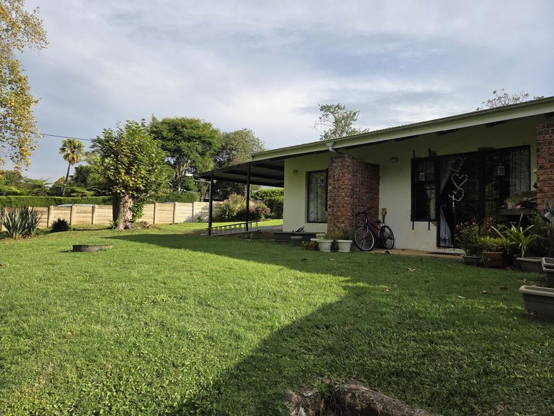Rear view of the house featuring a covered patio area, brick structural elements, and a spacious lawn with a boundary wall.
