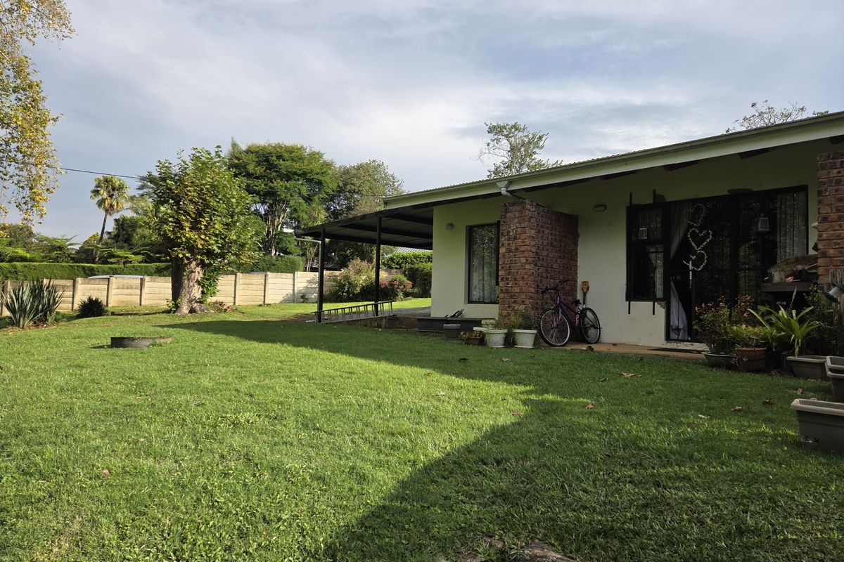Rear view of the house featuring a covered patio area, brick structural detailing, and a spacious garden with a concrete boundary wall.