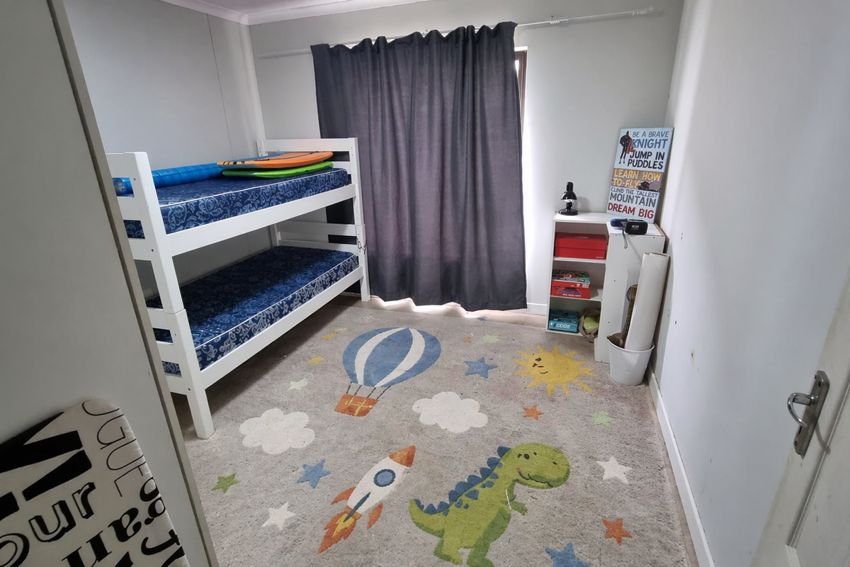 A functional bedroom featuring a window with curtain rail, suitable for use as a child's room or guest space.