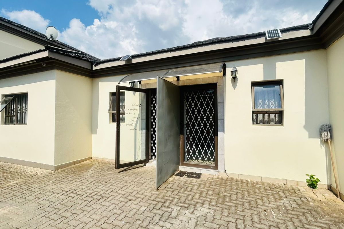 A paved rear courtyard area featuring security gates, an entrance awning, and external wall lighting, providing a functional outdoor space.