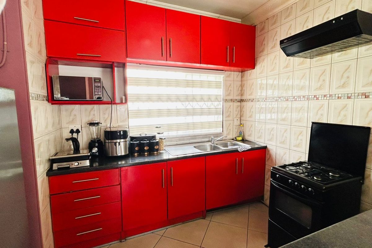 A functional kitchen featuring vibrant red cabinetry, tiled backsplash, stainless steel sink, and integrated extractor fan with tiled flooring.